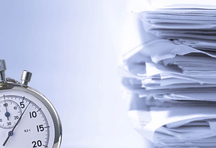close de um relógio com uma pilha de papeis ao fundo - Por que digitalizar os documentos da sua empresa