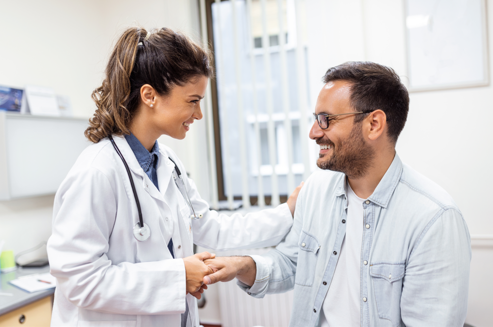 Médica e paciente em consultório dando um aperto de mão e sorrindo um para o outro