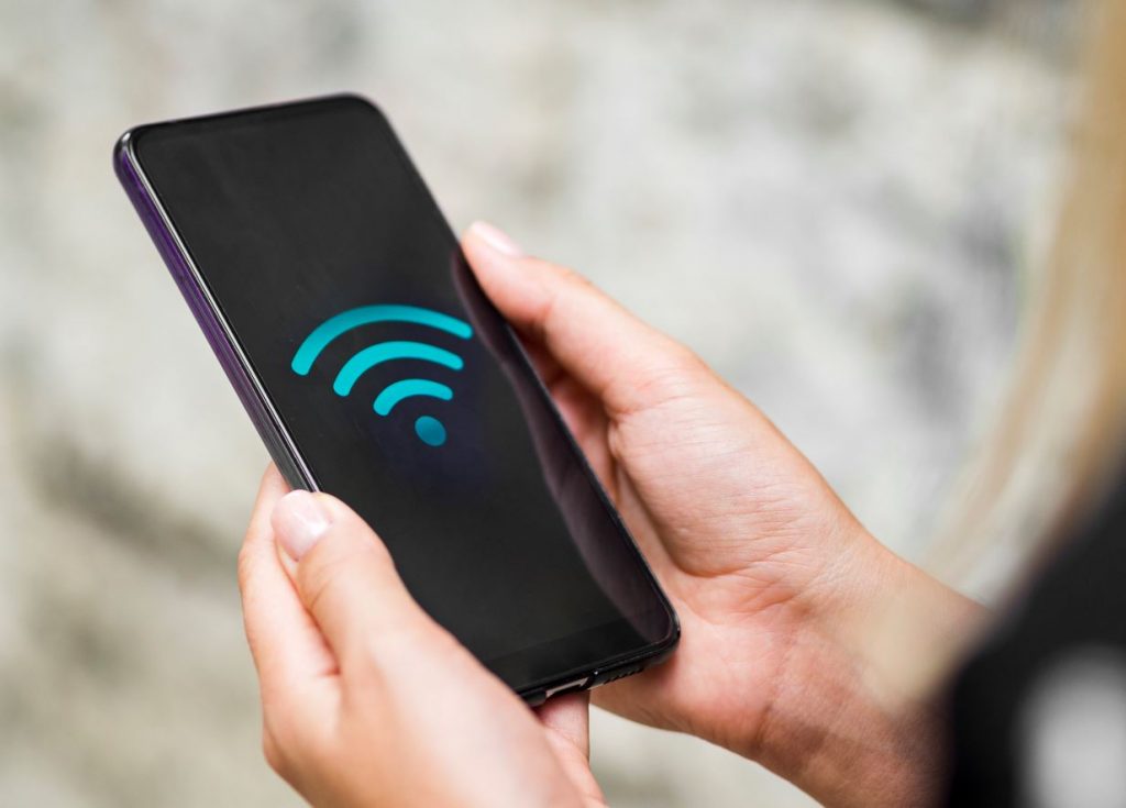 Foco na mão de uma pessoa segurando um smartphone cuja tela apresenta um símbolo de conexão Wi-Fi