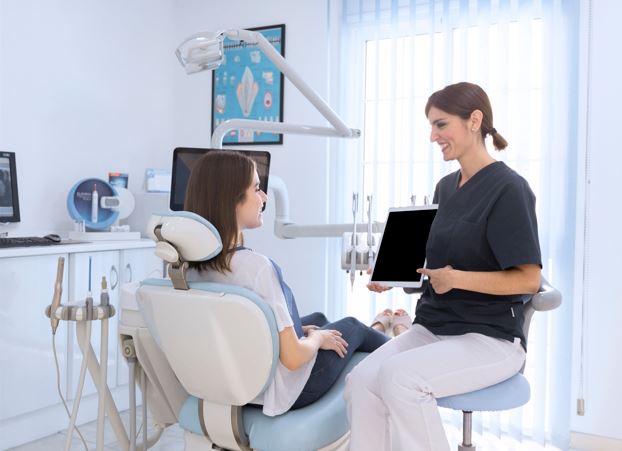 Em um consultório, dentista utiliza tablet para mostrar algo para paciente.