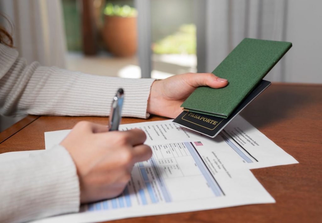 Foco nas mãos de uma mulher segurando um passaporte e fazendo assinatura em um papel sobre a mesa de madeira