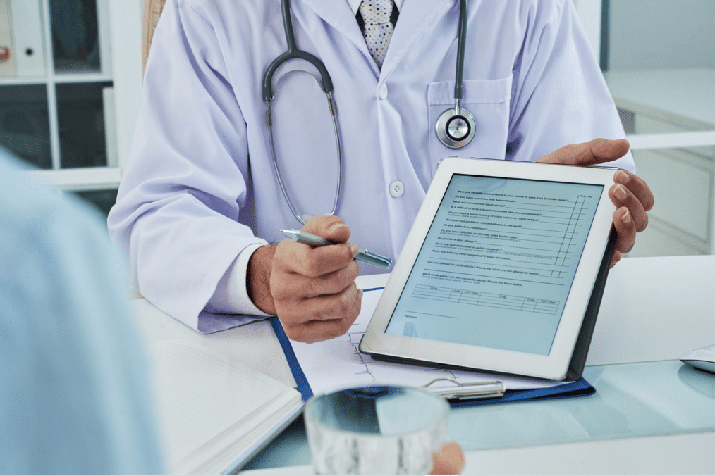 Médico segura tablet contendo formulário eletrônico indicando a paciente que faça assinatura digital.