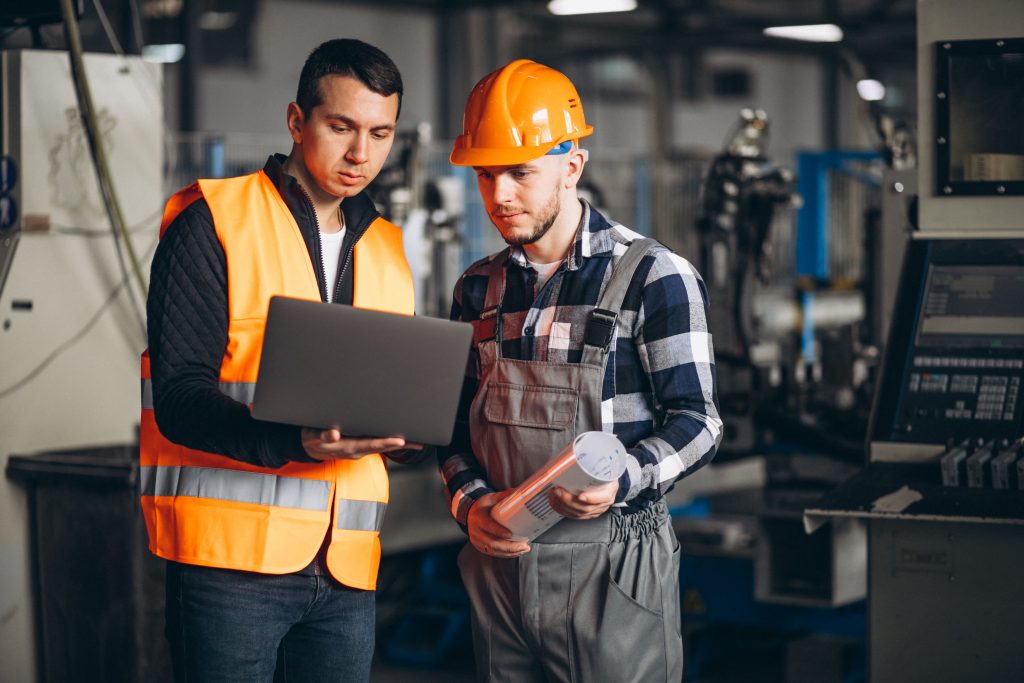 Dois homens engenheiros em ambiente industrial conversam e analisam informações no notebook representando gestão de documentos nas indústrias