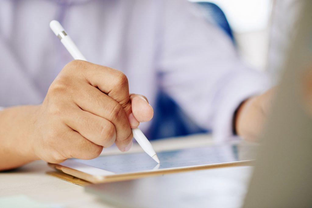 oco na mão de um homem usando uma caneta eletrônica em um tablet sobre uma mesa de escritório