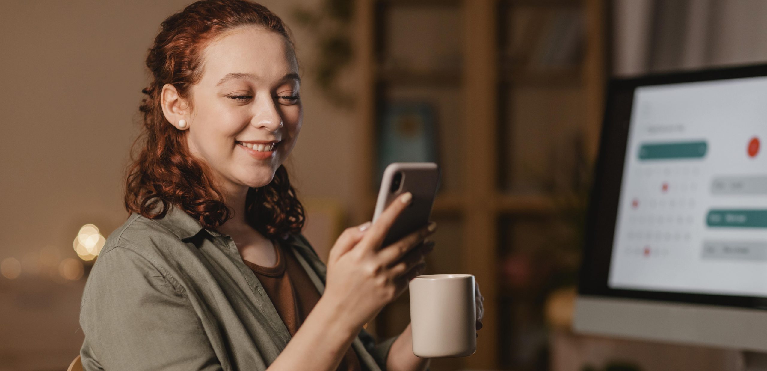 Jovem mulher segurando celular em uma mão e caneca em outra