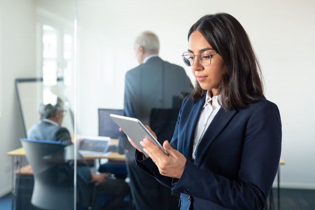 Mulher empresária em escritório segurando um tablet e utilizando sistema de gestão de qualidade.